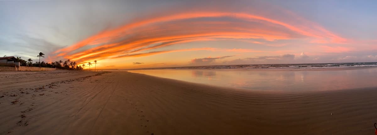 Zonsondergang op het strand van Guajiru, met kleurrijke wolken en kokospalmen langs de kust.