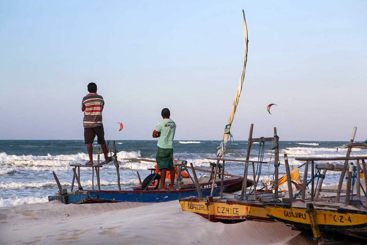Vissers naast jangadas (traditionele vissersvlotten) op het strand van Guajiru, met een boot waarop de naam van het dorp staat.